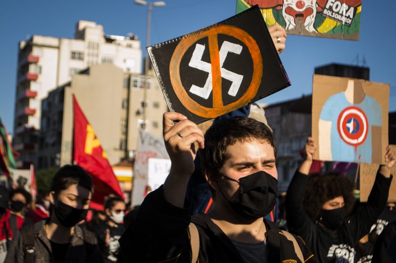 На передньому плані протестуючий у чорній масці тримає знак із перекресленою свастикою.
